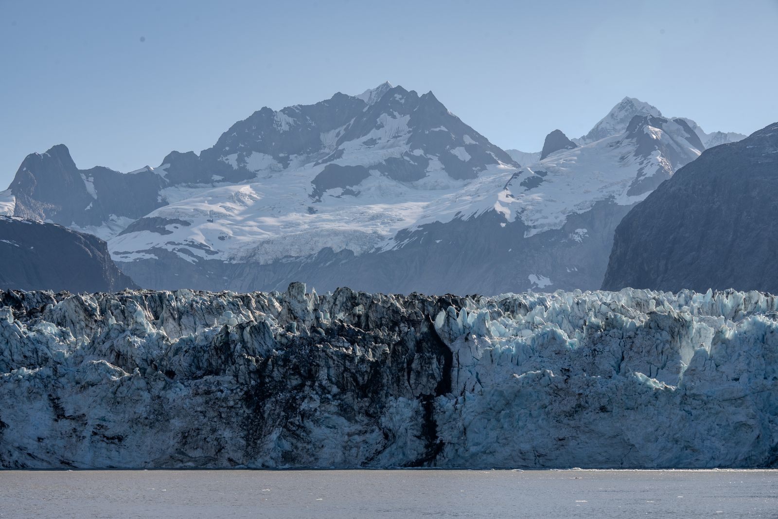 A tidewater glacier face beneath snowy peaks, the scenery that draws people to planning a cruise to Alaska