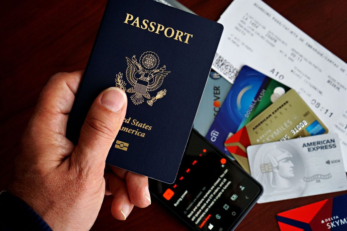 A hand holding a U.S. passport above payment cards and a phone