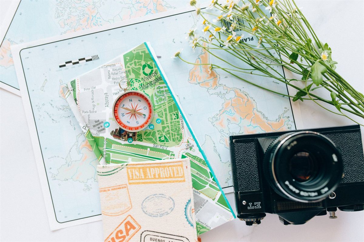 A compass, folded maps, a passport visa stamp and a camera laid out on a table