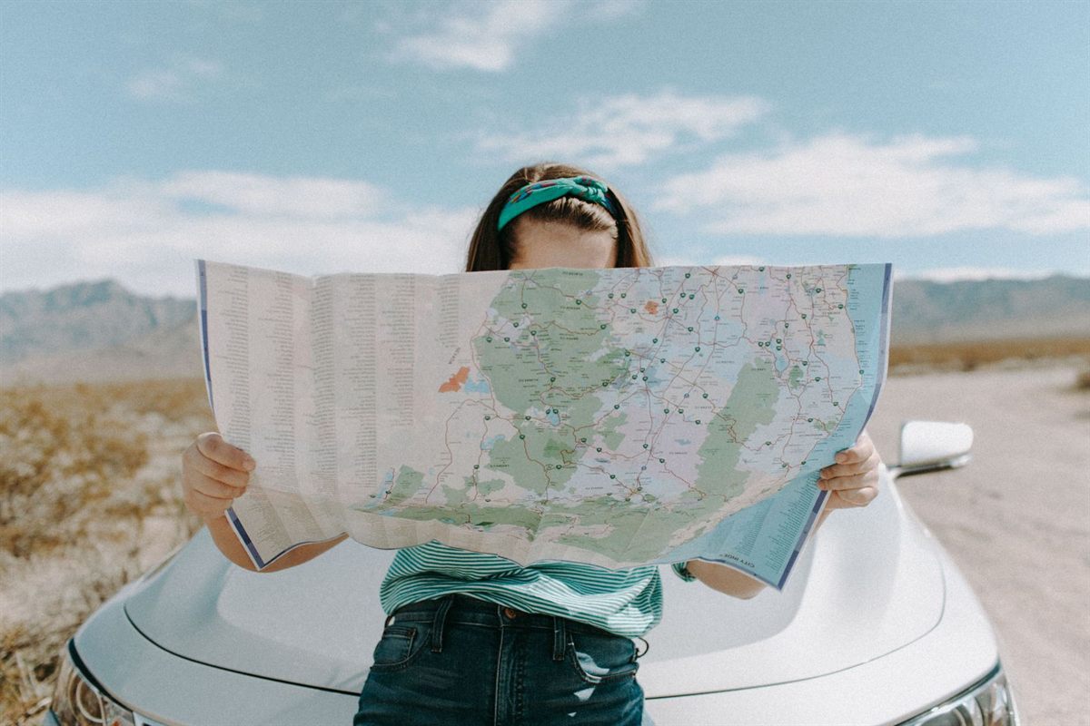 A traveler leaning on a car holds open a large road map in a desert landscape