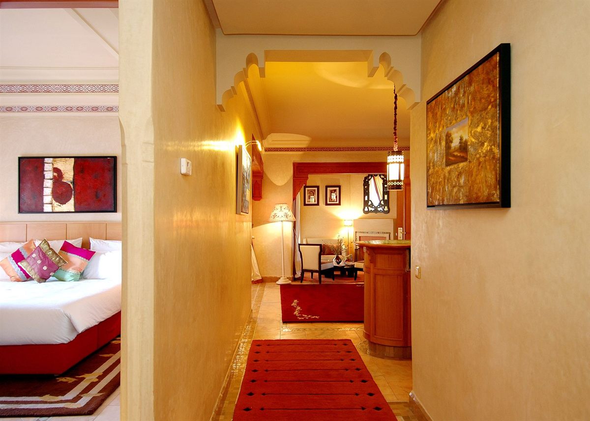 A warm hotel corridor leading to a guest room with a red carpet runner
