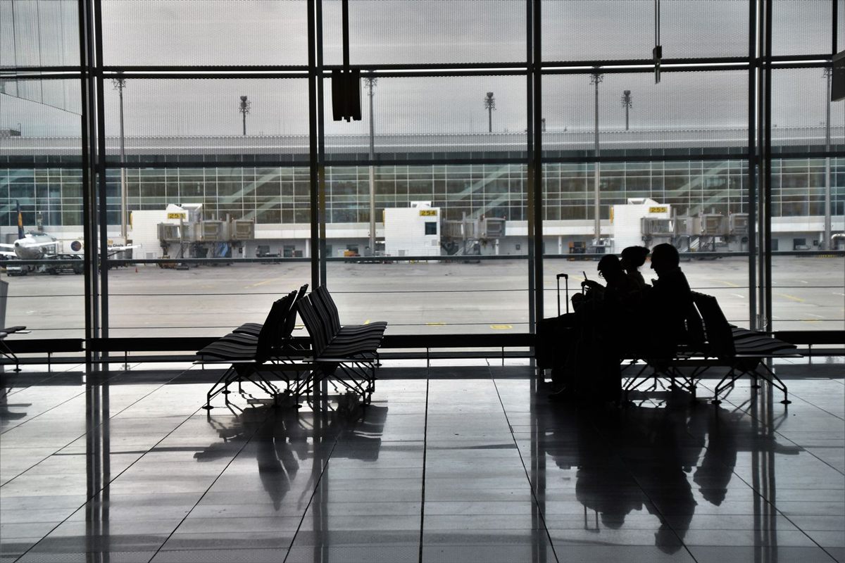 Silhouettes of travelers waiting on seats by tall airport windows