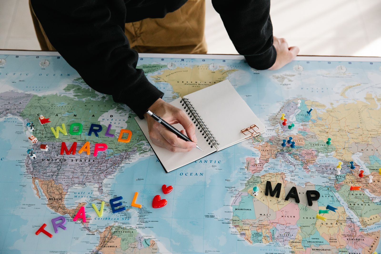A traveler writing notes on a world map with letters spelling travel, ready to plan a cruise for 2027