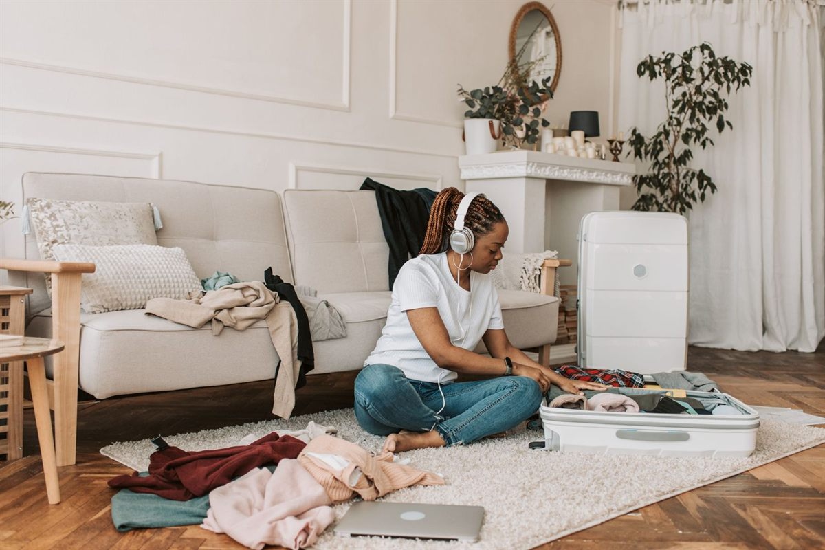 A woman with headphones packing a suitcase on a living room rug